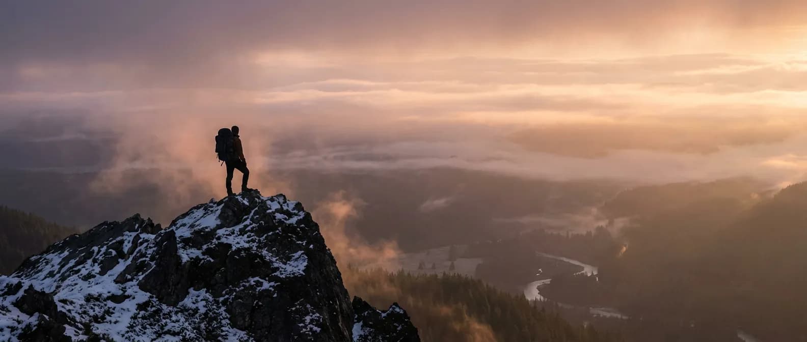 Un voyageur solitaire au sommet d'une montagne admirant un paysage grandiose au lever du soleil.