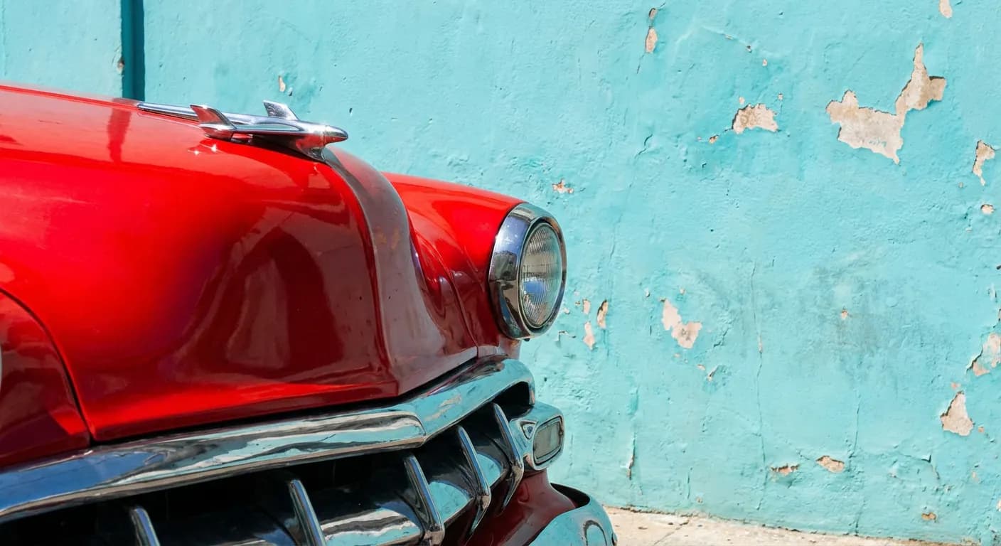 Gros plan iconique d'une voiture ancienne rouge devant un mur bleu turquoise à Cuba.