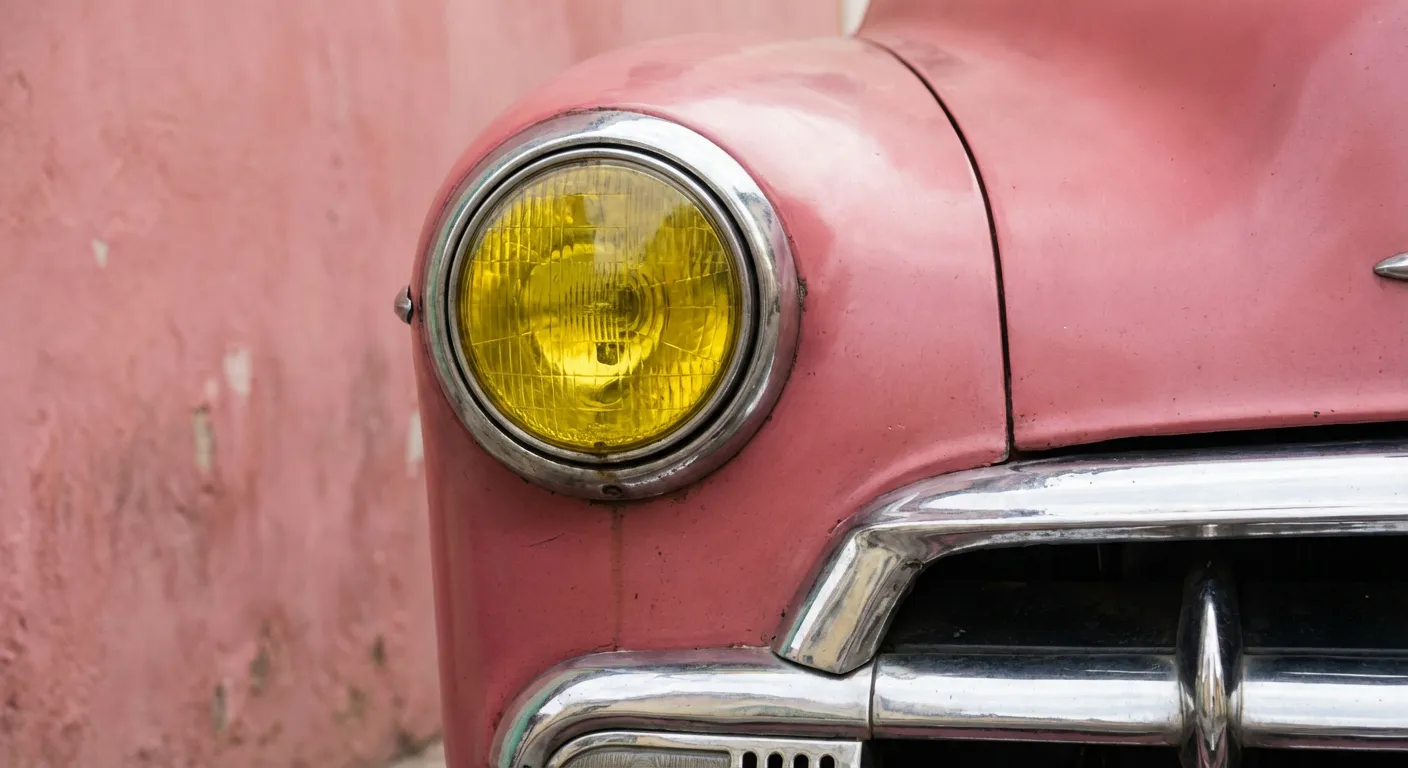 Détail d'une voiture vintage jaune devant un mur rose typique de Cuba
